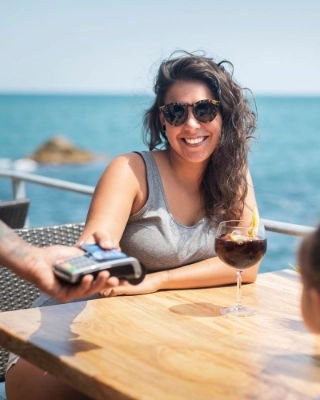 Eine junge Frau bezahlt im Ausland am Meer mit der Debit- oder Kreditkarte.